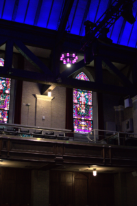 A pink and green stained glass window stands out in the dim light of the Scottish Rite Theatre